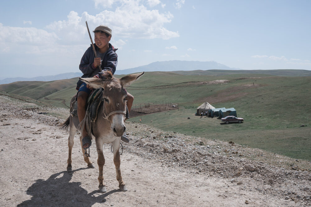 A young herder rides through the hills with camp in the distance.