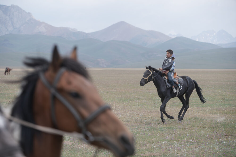 Two boys share a horse on the open plain.