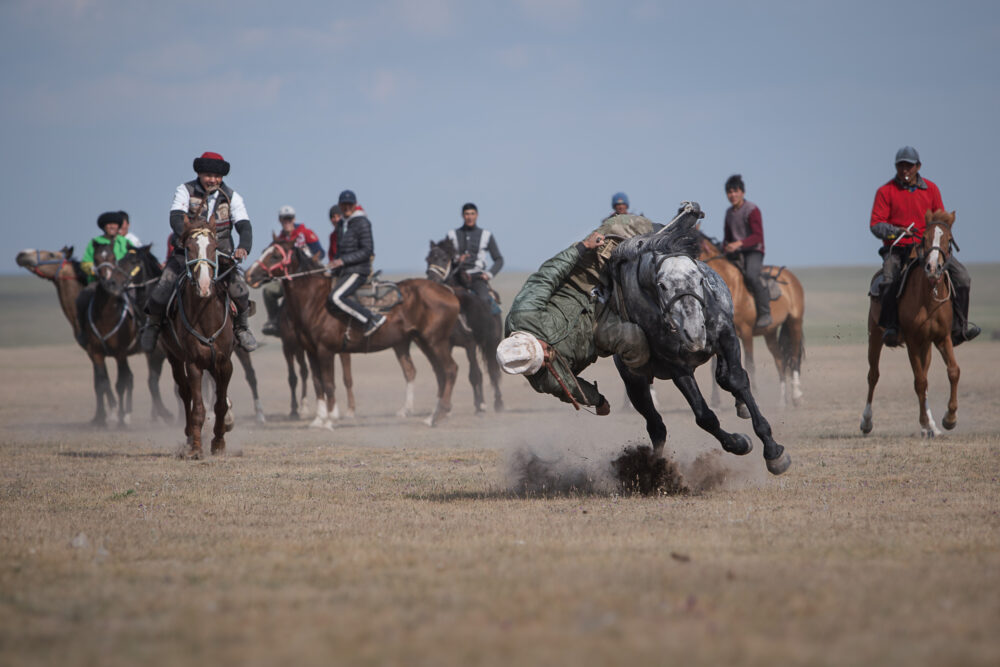 A rider leans down at full speed to grab money from the ground.