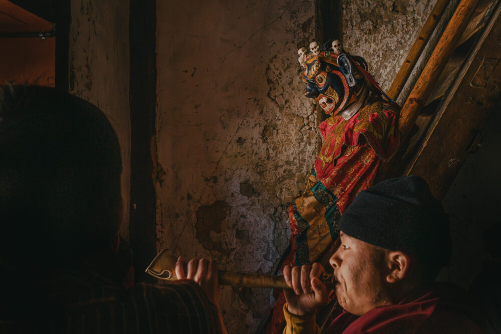 A masked figure waits in the shadows, the performance not yet begun.