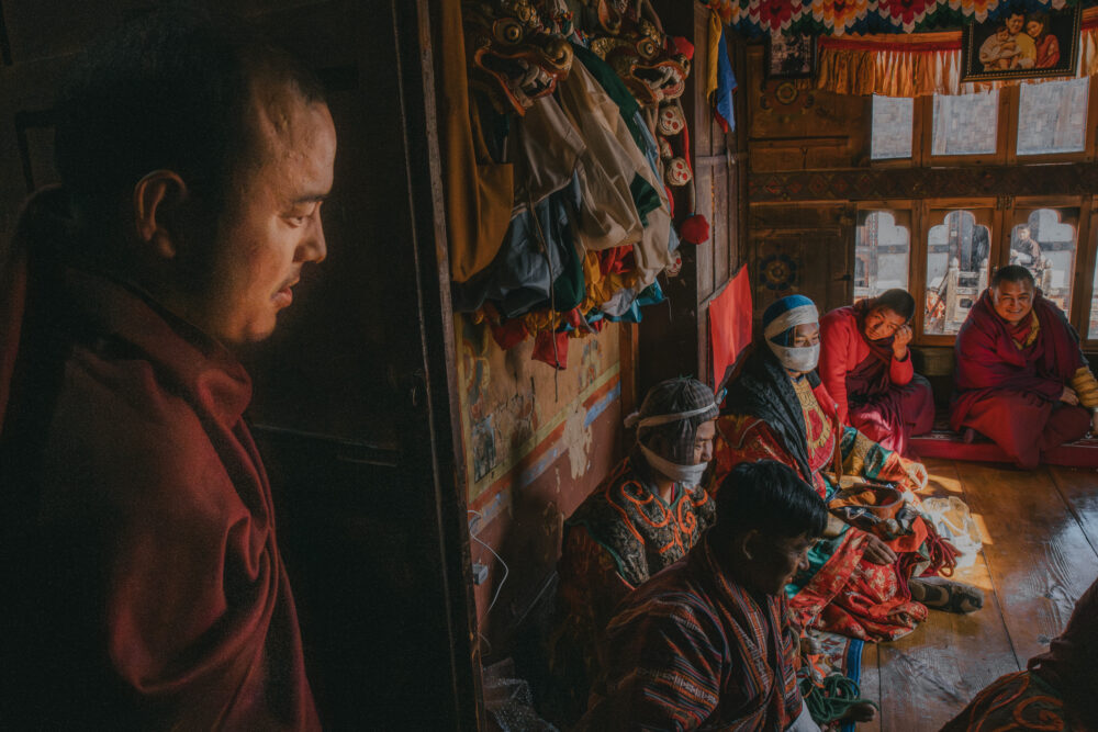 Behind the scenes, dancers and monks sit quietly, a pause between performances in a room filled with colour and calm.