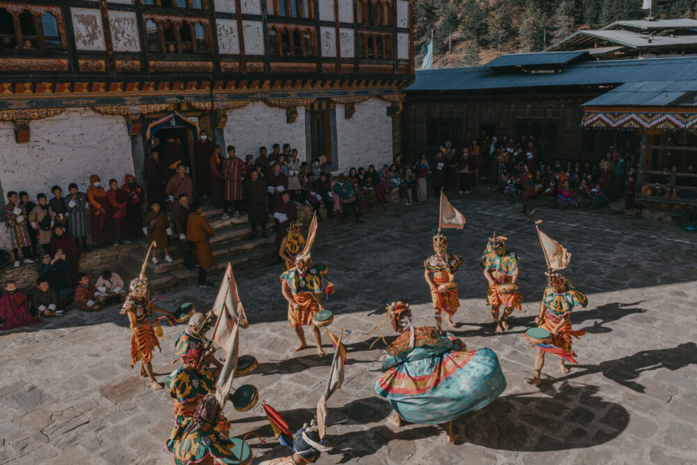 The courtyard fills with movement and shadow as dancers circle, the audience gathered closely around the edge.