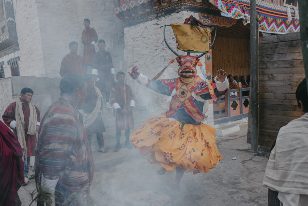 A dancer steps forward through smoke, emerging from the ritual space.